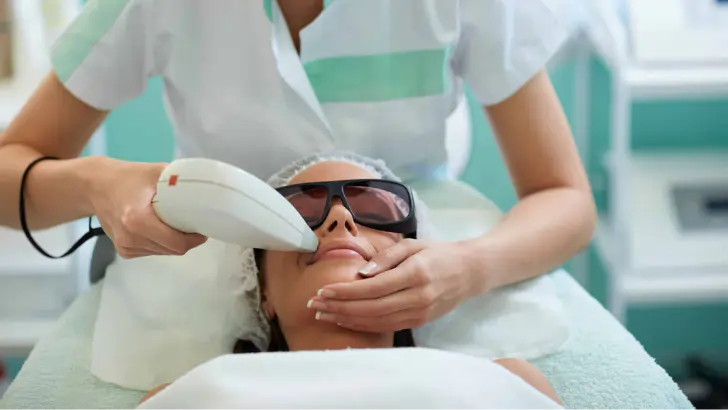 Esthetician performing a laser facial treatment on a client wearing protective goggles, illustrating pay by bank for health and wellness.