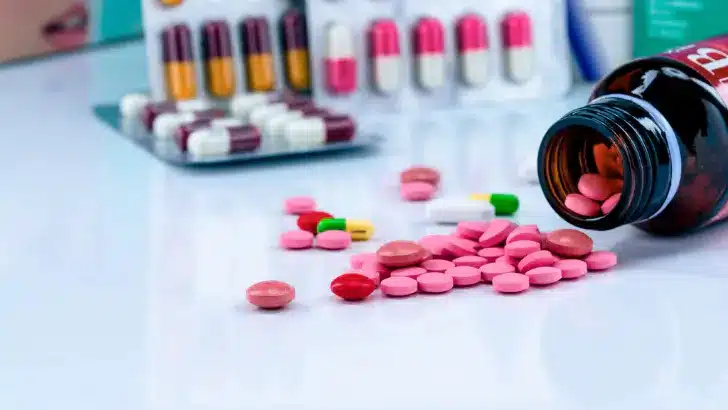 Assorted pink and multicolored pills spilled from a bottle next to blister packs of medication, illustrating pay by bank for pharmacies.