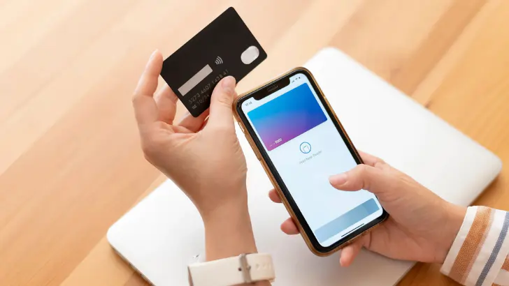 Customer holding a contactless credit card in one hand and a smartphone showing a digital wallet payment screen in the other.