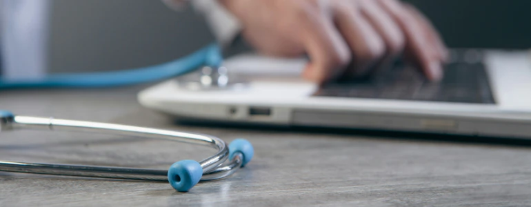 Stethoscope resting on a desk next to a person typing on a laptop, illustrating payment processing for digital health and healthcare platforms.