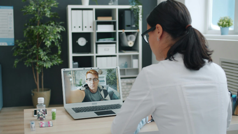 Doctor in a white coat conducting a remote video consultation with a patient on a laptop, illustrating recurring care programs and remote consultations for healthcare businesses.